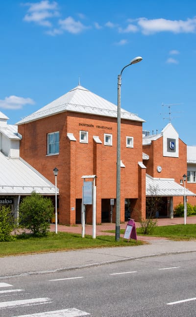 The red-brick Enontekioe municipal office building with white roofs beside a roadside on a clear summer day.