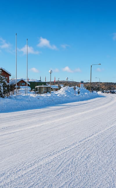 Snow-covered village street in Inari, Finnish Lapland, with a Sale store and low buildings under blue sky.