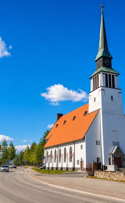 White stone church with a green copper spire beside a curving street in Kemijarvi, Finland