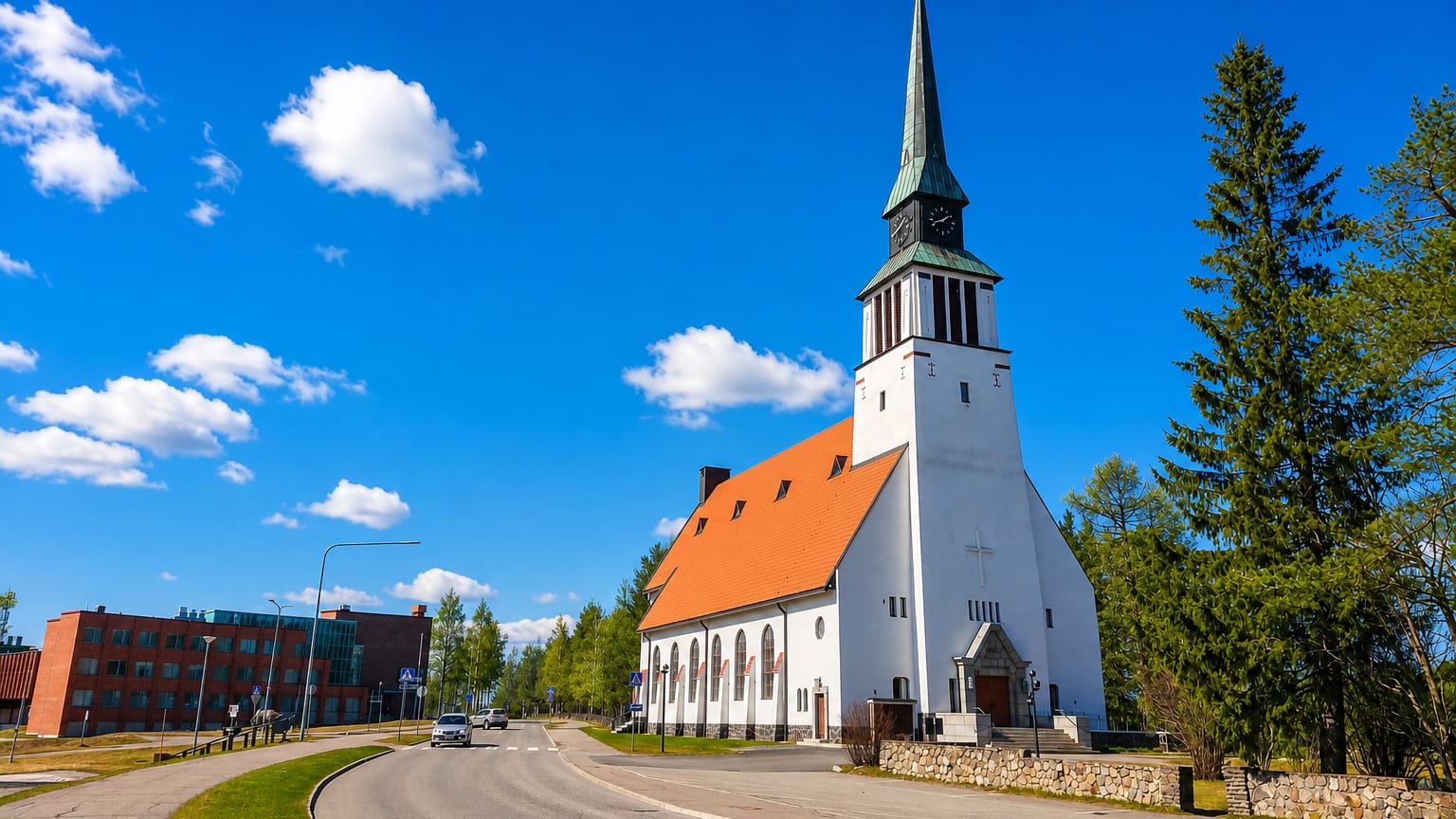 White stone church with a green copper spire beside a curving street in Kemijarvi, Finland