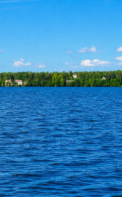 Calm blue water leading to Keminmaa's forested shoreline and a distant white church tower under a bright summer sky.