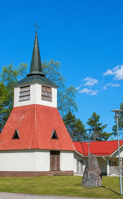 White and red wooden bell tower church beside a lake among birch trees in Posio, Finland.