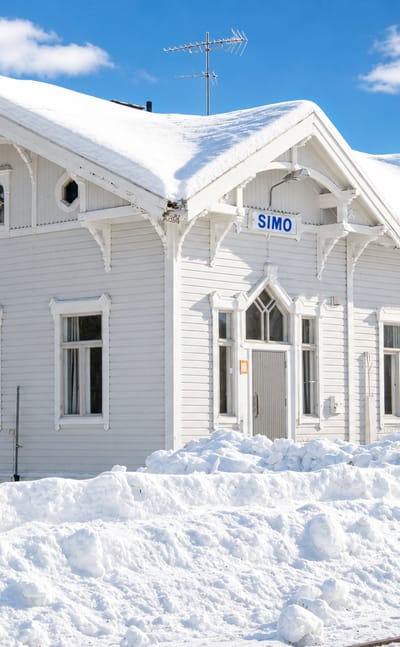 Simo's white wooden railway station under deep snow, with its clear SIMO nameboard and blue sky.