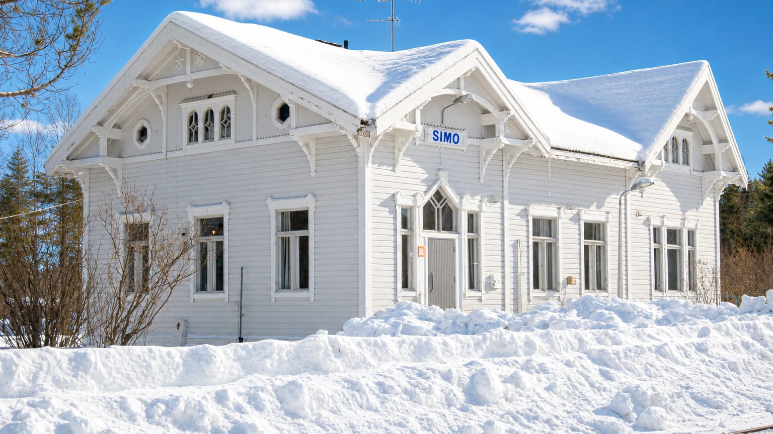 Simo's white wooden railway station under deep snow, with its clear SIMO nameboard and blue sky.