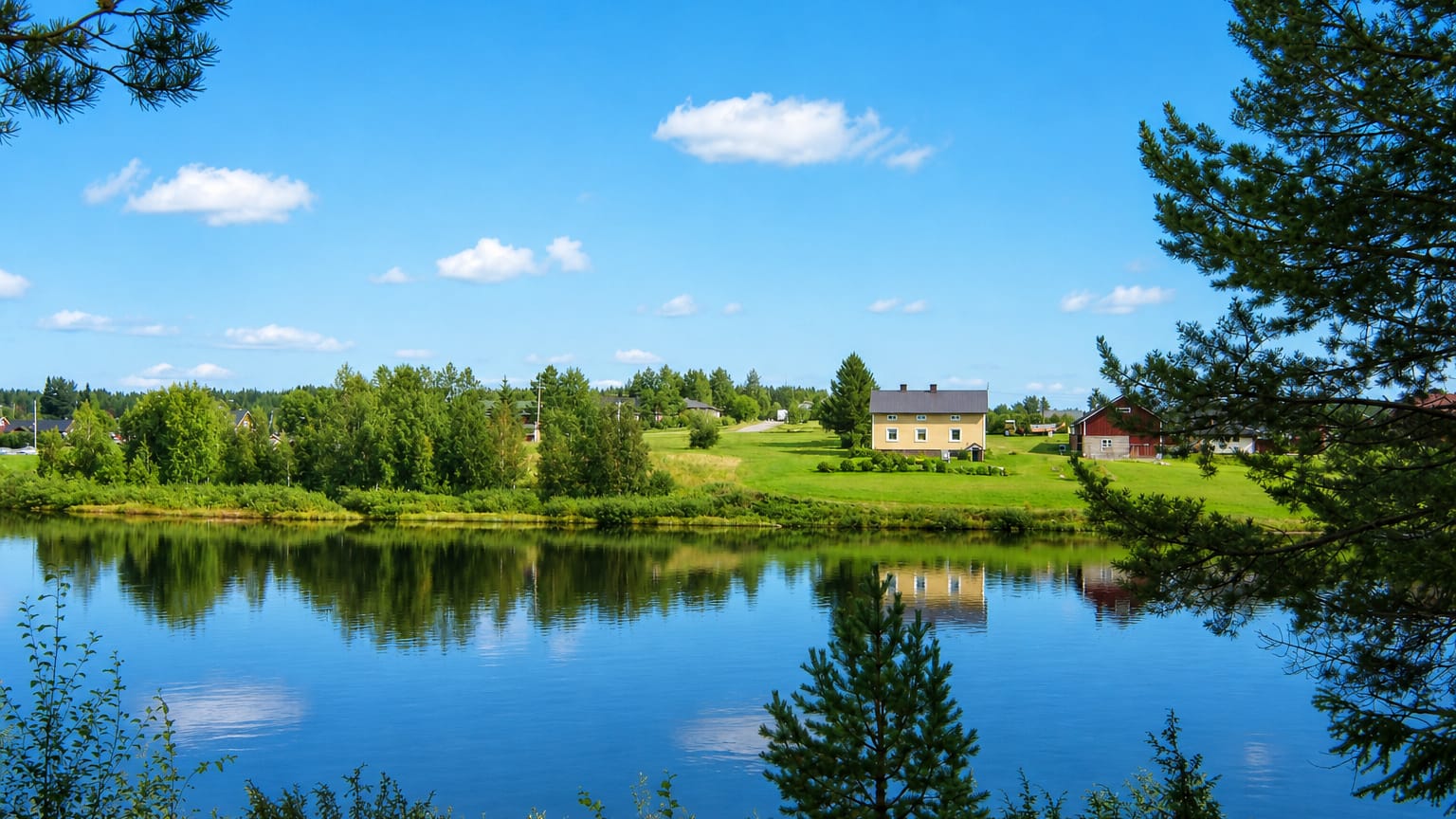 A calm river reflecting a yellow farmhouse and red barn among pine forest near Sodankylae in Finnish Lapland.