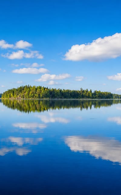 Calm forest-fringed lake reflecting blue sky and white clouds near Hartola, Finland.
