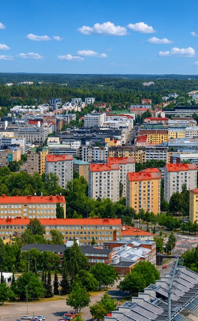 Aerial daytime view over Lahti, Finland, with colourful apartment blocks, green parkland and a sports arena ringed by forest