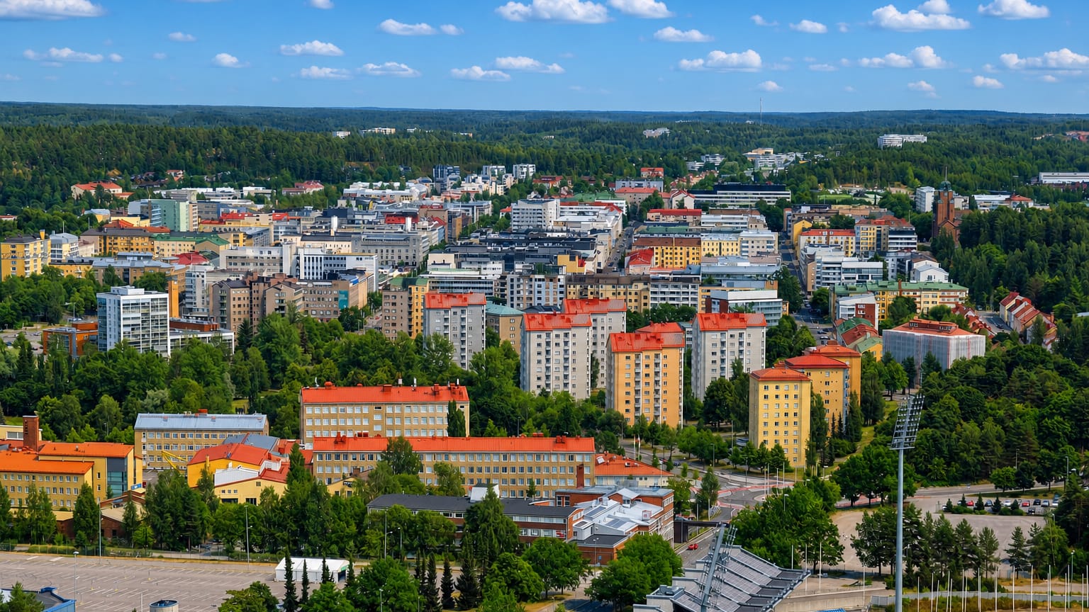 Aerial daytime view over Lahti, Finland, with colourful apartment blocks, green parkland and a sports arena ringed by forest