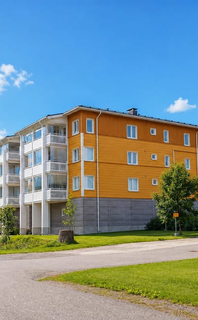 Yellow timber-clad apartment block backed by spruce forest in Laune, a residential district of Lahti.