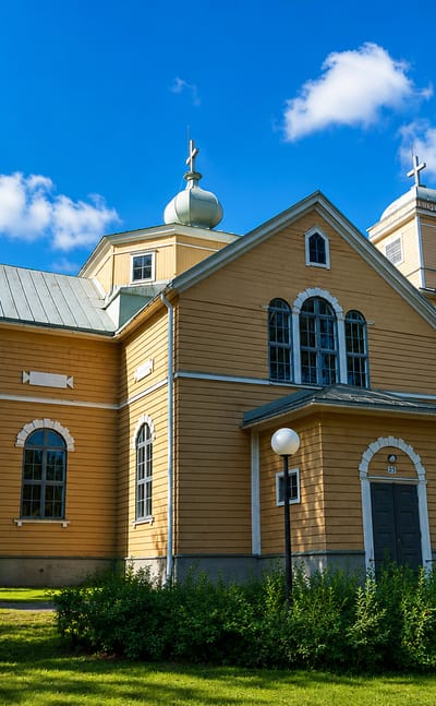Orimattila's large ochre wooden church with a domed tower framed by birch trees.