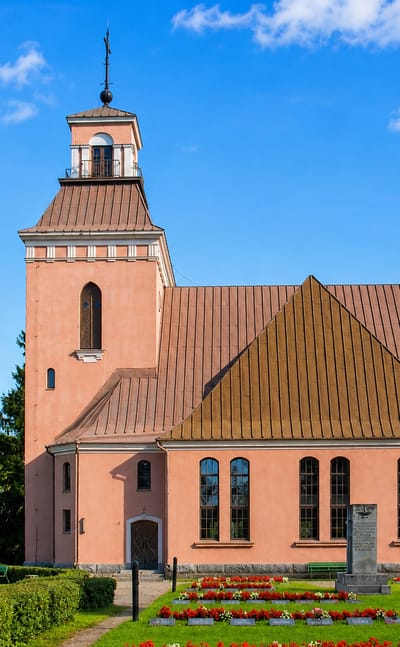 Padasjoki's salmon-pink church with a brown belltower and copper roof above a flowered churchyard