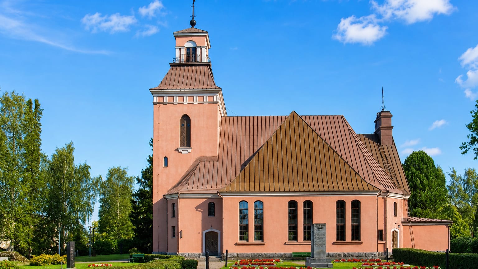 Padasjoki's salmon-pink church with a brown belltower and copper roof above a flowered churchyard