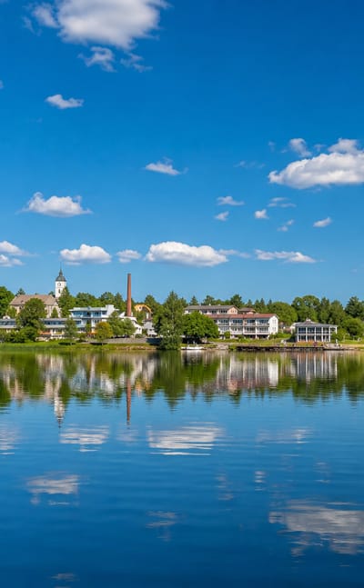 Lakeside skyline of Sysmä, Finland, with a church spire and waterfront buildings reflected in calm blue water.