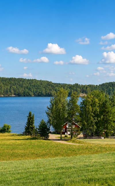 The rolling lake-and-field national landscape with a red cottage in Hämeenkyrö, Finland.