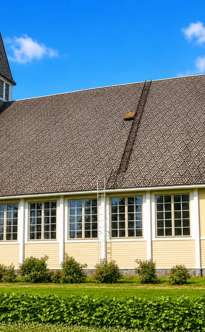 Yellow wooden church with a shingled spire on a green lawn in Kihniö, Finland, under a blue sky.