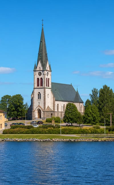 Waterfront view of Kuhmoinen, Finland, with its stone church spire and water tower above the lakeshore.