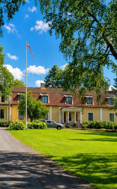 Yellow manor house with a flagpole and gravel drive amid lawns and trees at Kylmäkoski, Finland.