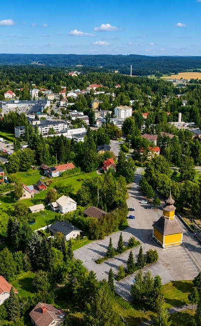 Aerial view of Orivesi, Finland, its yellow wooden bell tower rising amid low-rise buildings and surrounding boreal forest.