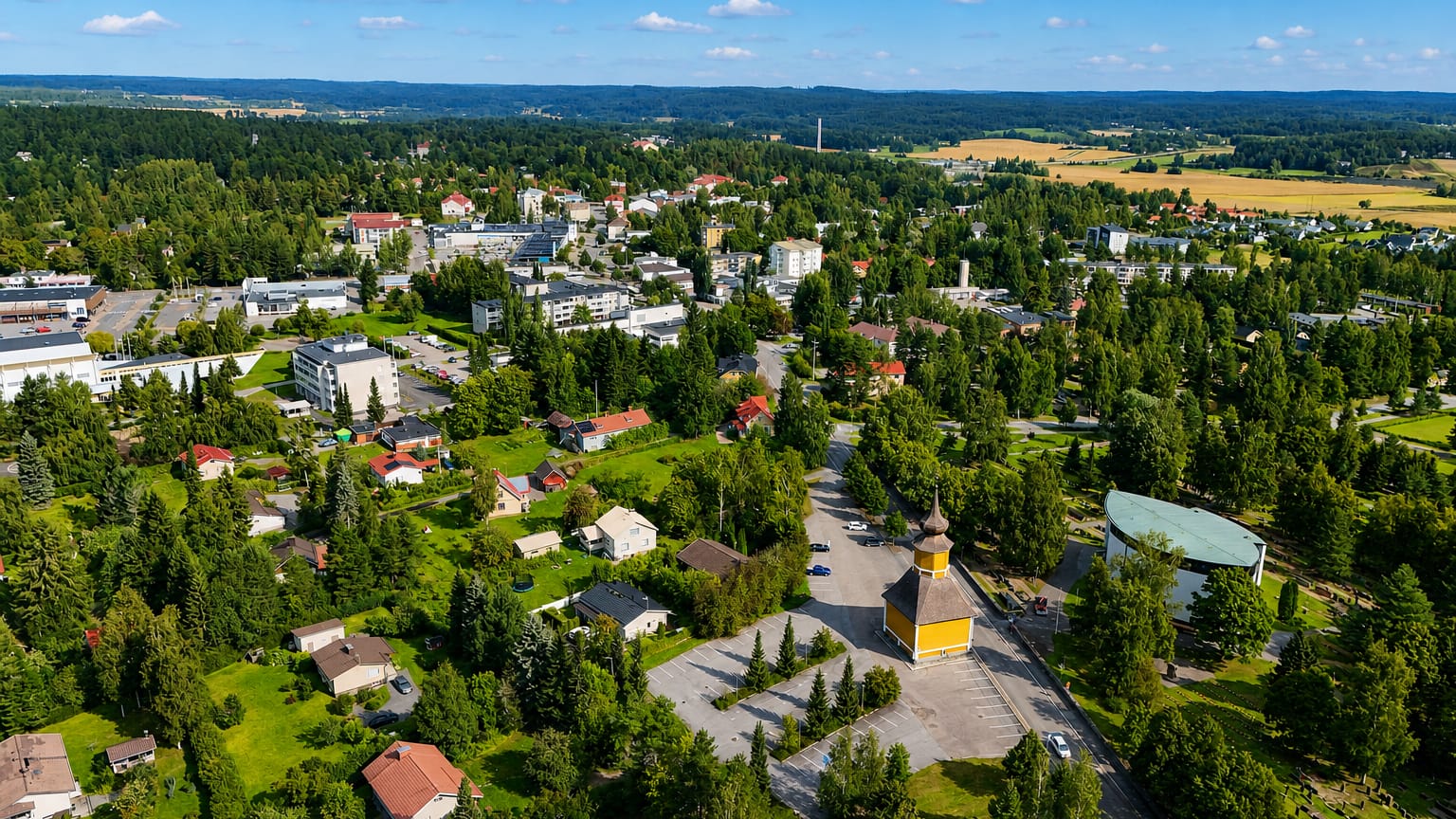 Aerial view of Orivesi, Finland, its yellow wooden bell tower rising amid low-rise buildings and surrounding boreal forest.