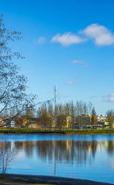 Calm lake reflecting Parkano's low-rise apartment and commercial buildings beneath a blue Finnish spring sky.