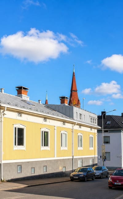 Yellow wooden house and white functionalist block at Juhannuskyla in Tampere, church spire behind in autumn