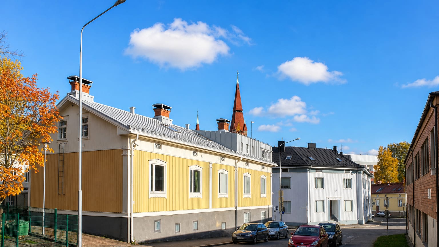 Yellow wooden house and white functionalist block at Juhannuskyla in Tampere, church spire behind in autumn