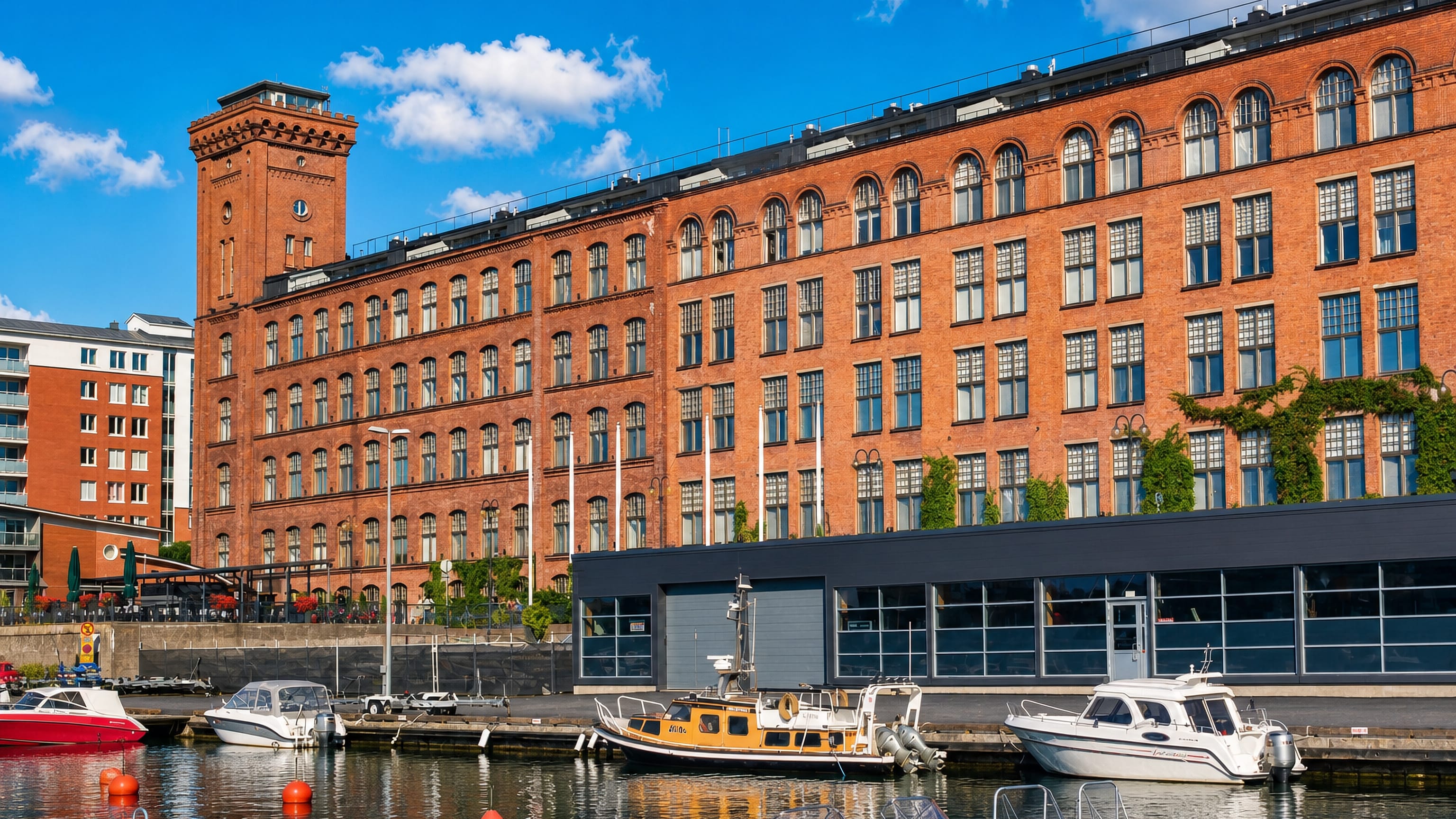 Red-brick former cotton mill and its tower rising above the lakeside marina at Lapinniemi, Tampere.