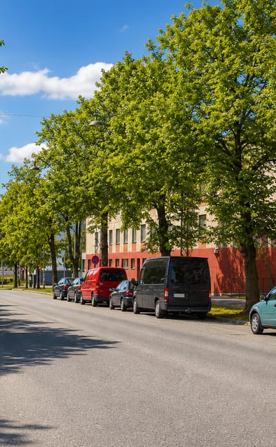 Tree-lined residential street with parked cars beside a red apartment block in Osmonmäki, Tampere.