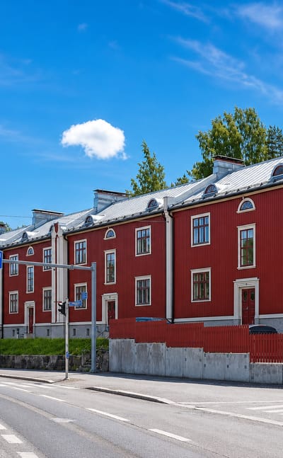 Long red timber terrace housing on a corner at Pyynikinrinne in Tampere, with pine woods behind.