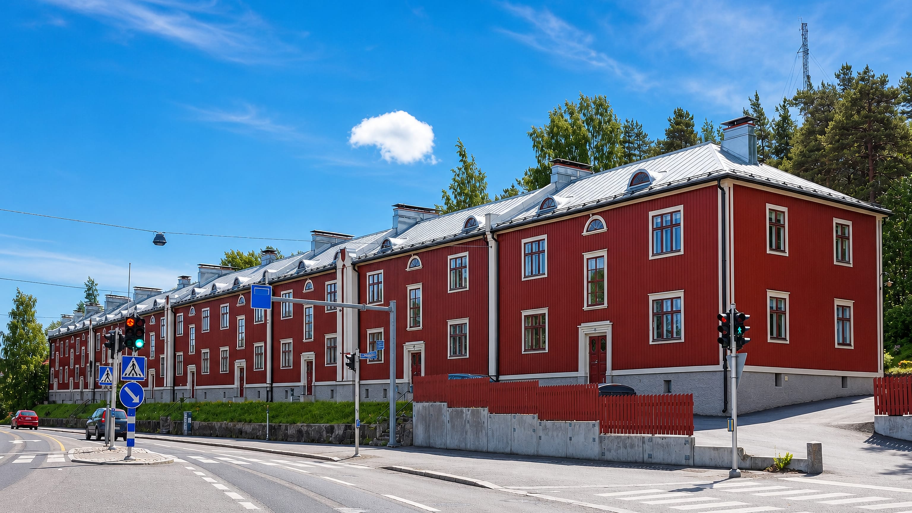 Long red timber terrace housing on a corner at Pyynikinrinne in Tampere, with pine woods behind.