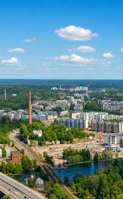 Aerial daytime view of Tampella, Tampere, with its red-brick factory chimney, lakeside waterfront and modern apartment blocks.