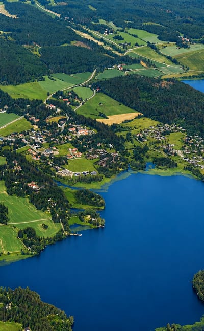 Aerial view of Vesilahti, Finland: a small lakeside village set among green farmland and forests beside a deep blue lake.