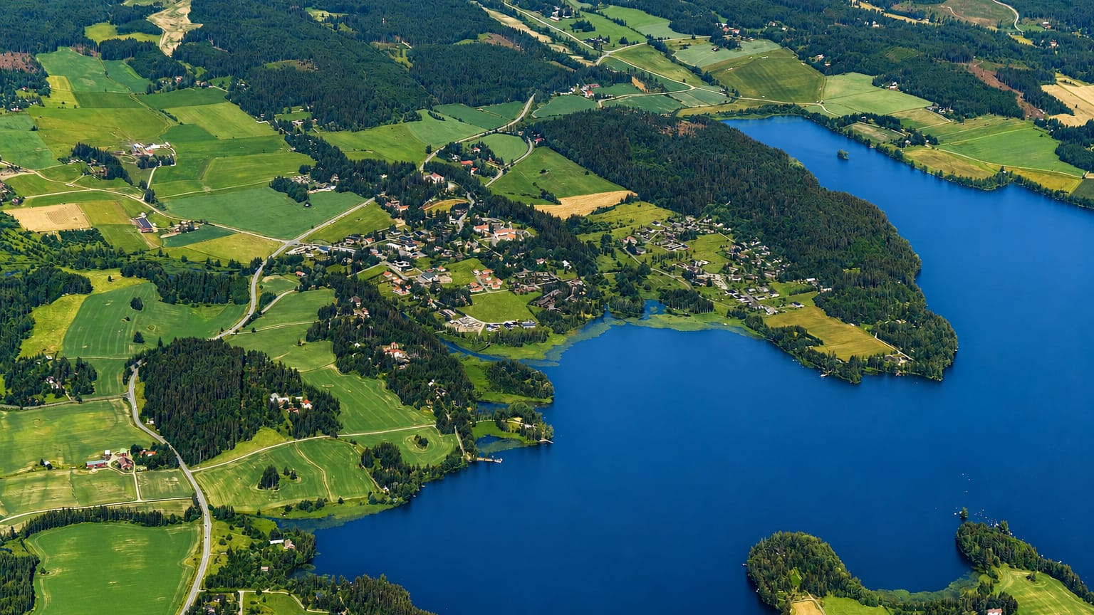 Aerial view of Vesilahti, Finland: a small lakeside village set among green farmland and forests beside a deep blue lake.