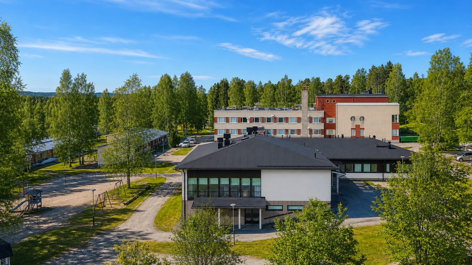 Aerial view of Virrat, Finland, showing a multi-storey building among birch trees with a forested horizon under clear blue sky.