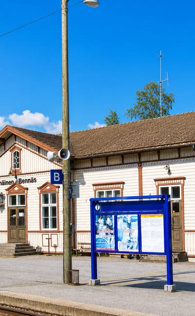 The wooden Bennas railway station with bilingual Pannainen-Bennas signage and platform on a sunny day.