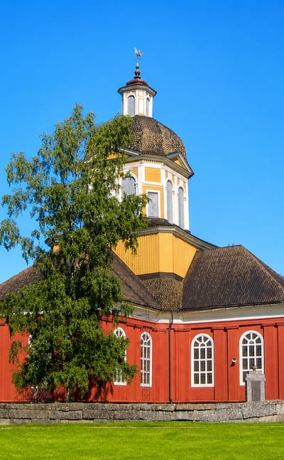 Red wooden church with an octagonal domed roof and yellow lantern tower behind a stone wall in Larsmo, Finland.