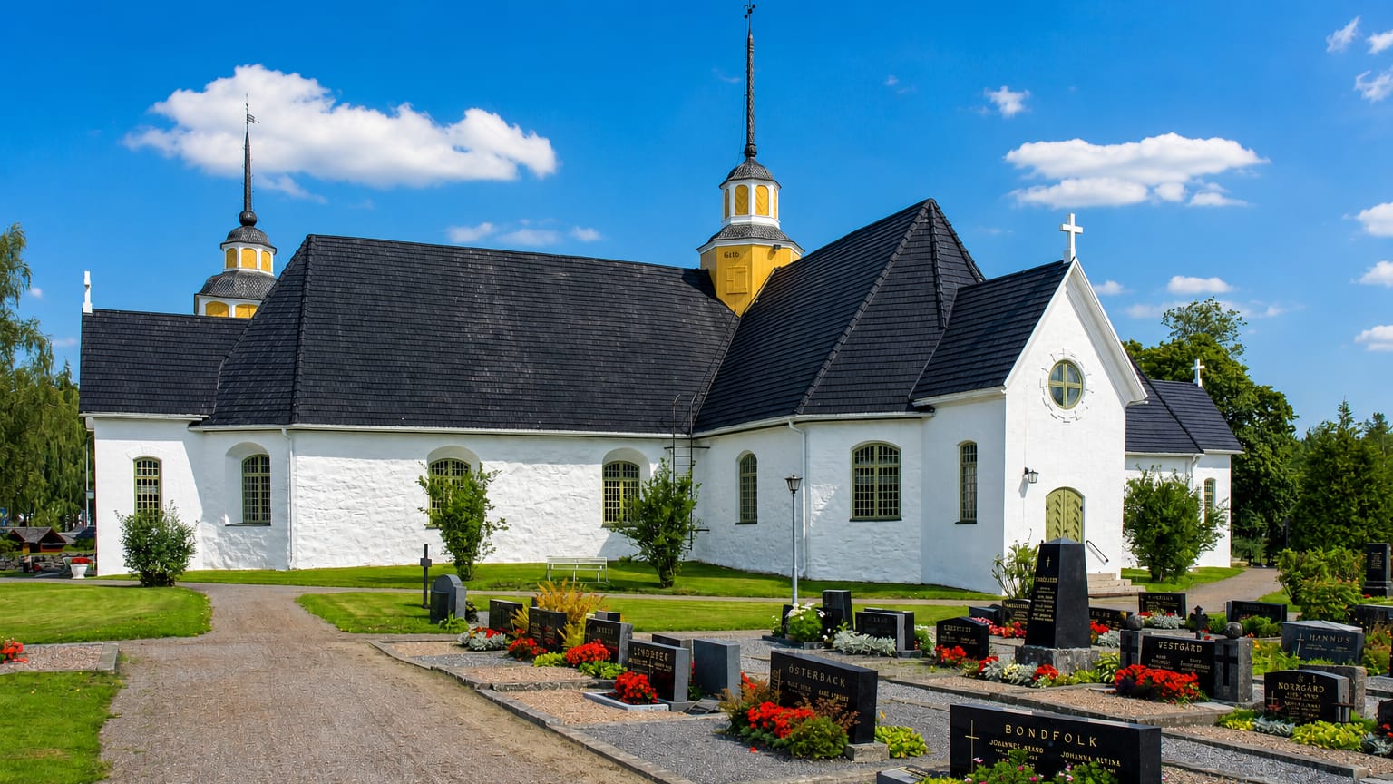 White stone church with two yellow-domed towers and a graveyard in Narpes, Finland, under a blue sky.