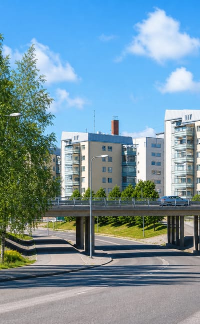 Road bridge and pale apartment blocks framed by summer birches in Hietalahti, Vaasa.