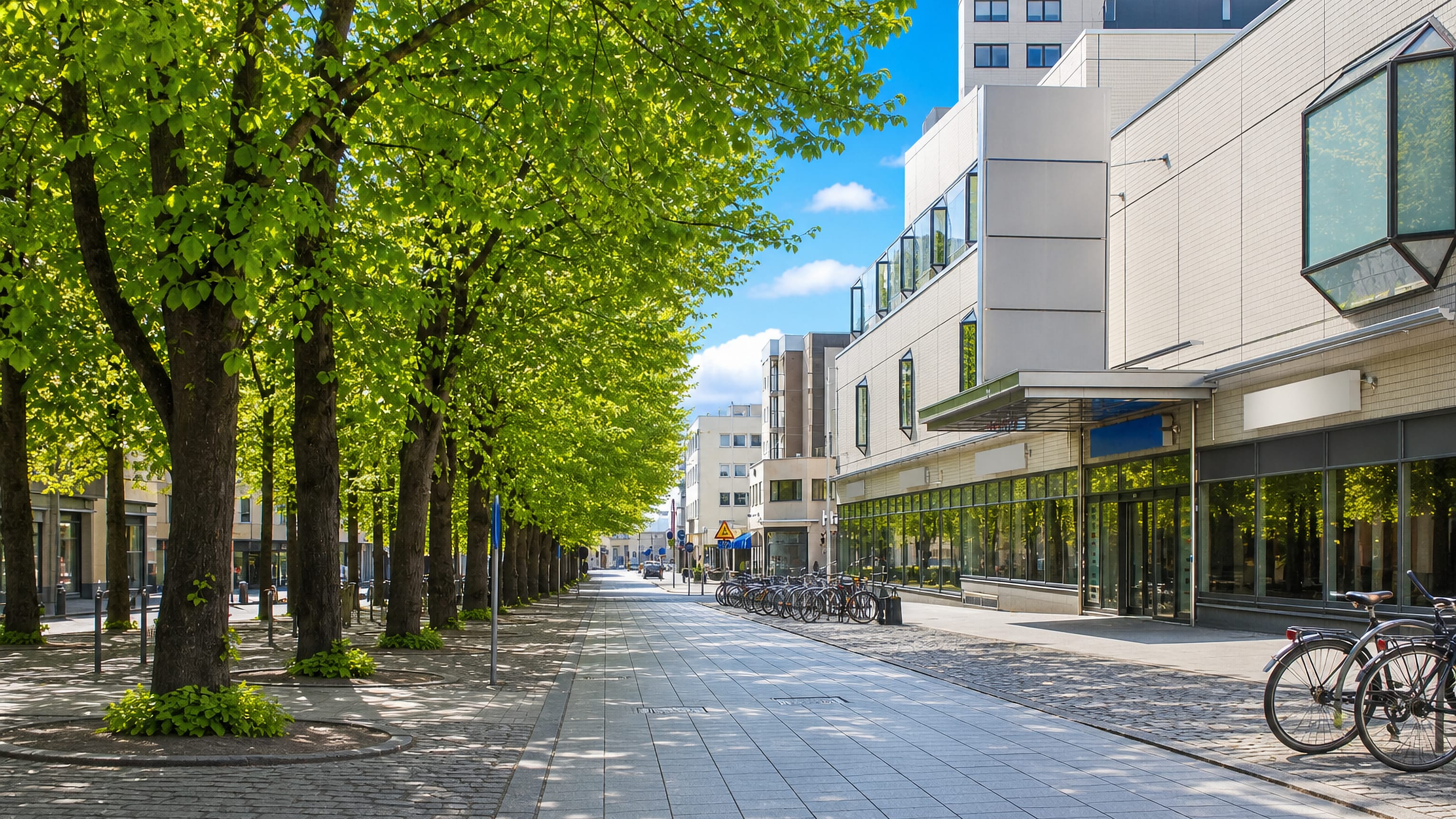 Lime-tree avenue and modern shopfronts along a paved pedestrian street in I kaupunginosa, central Vaasa.