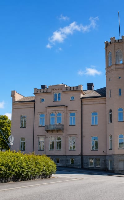 Historic pink stone building with a crenellated corner tower on a quiet street in II kaupunginosa, Vaasa.