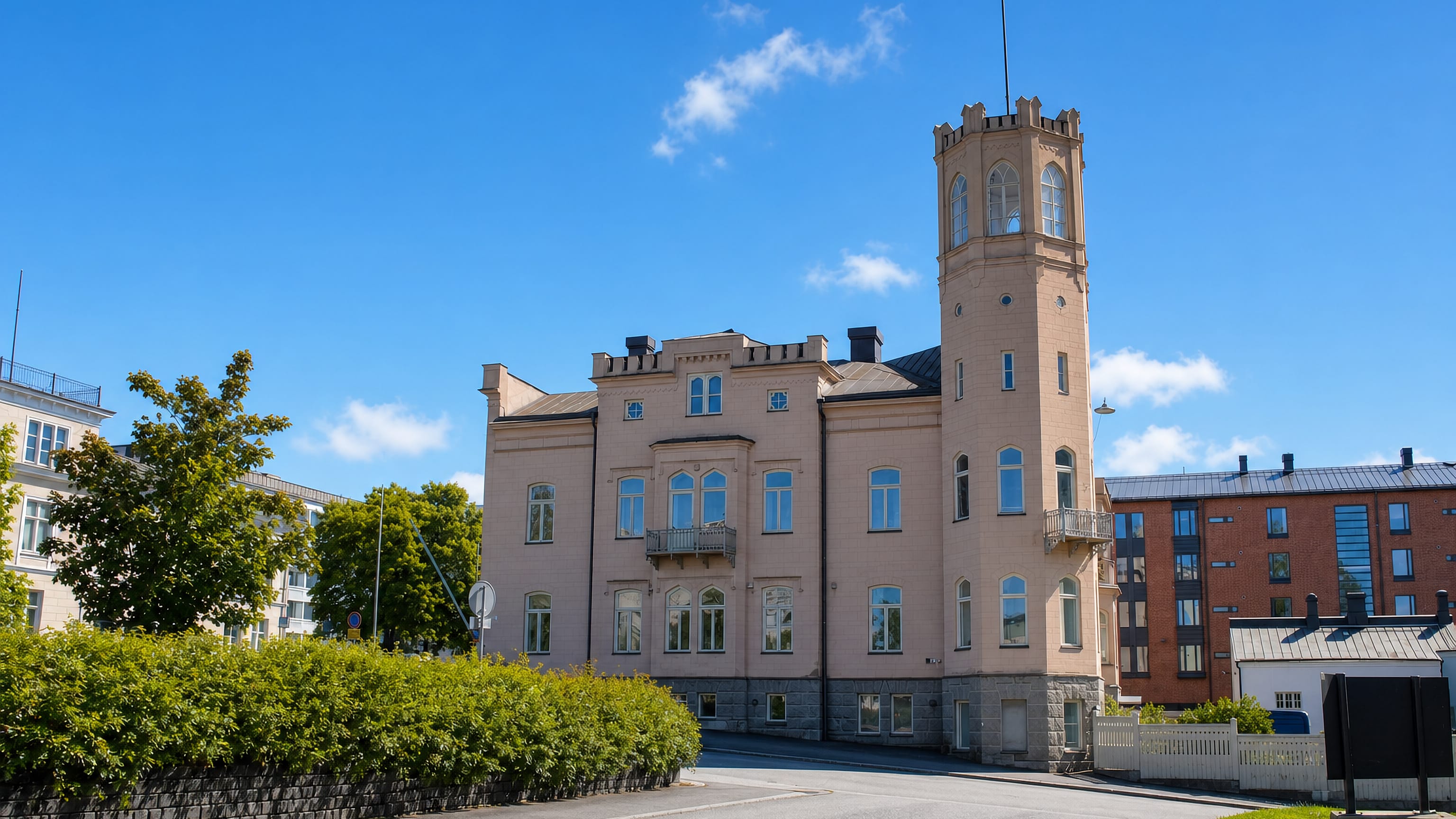Historic pink stone building with a crenellated corner tower on a quiet street in II kaupunginosa, Vaasa.