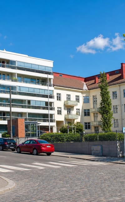 Modern white apartment block beside older cream flats on a cobbled corner in VI kaupunginosa, Vaasa.