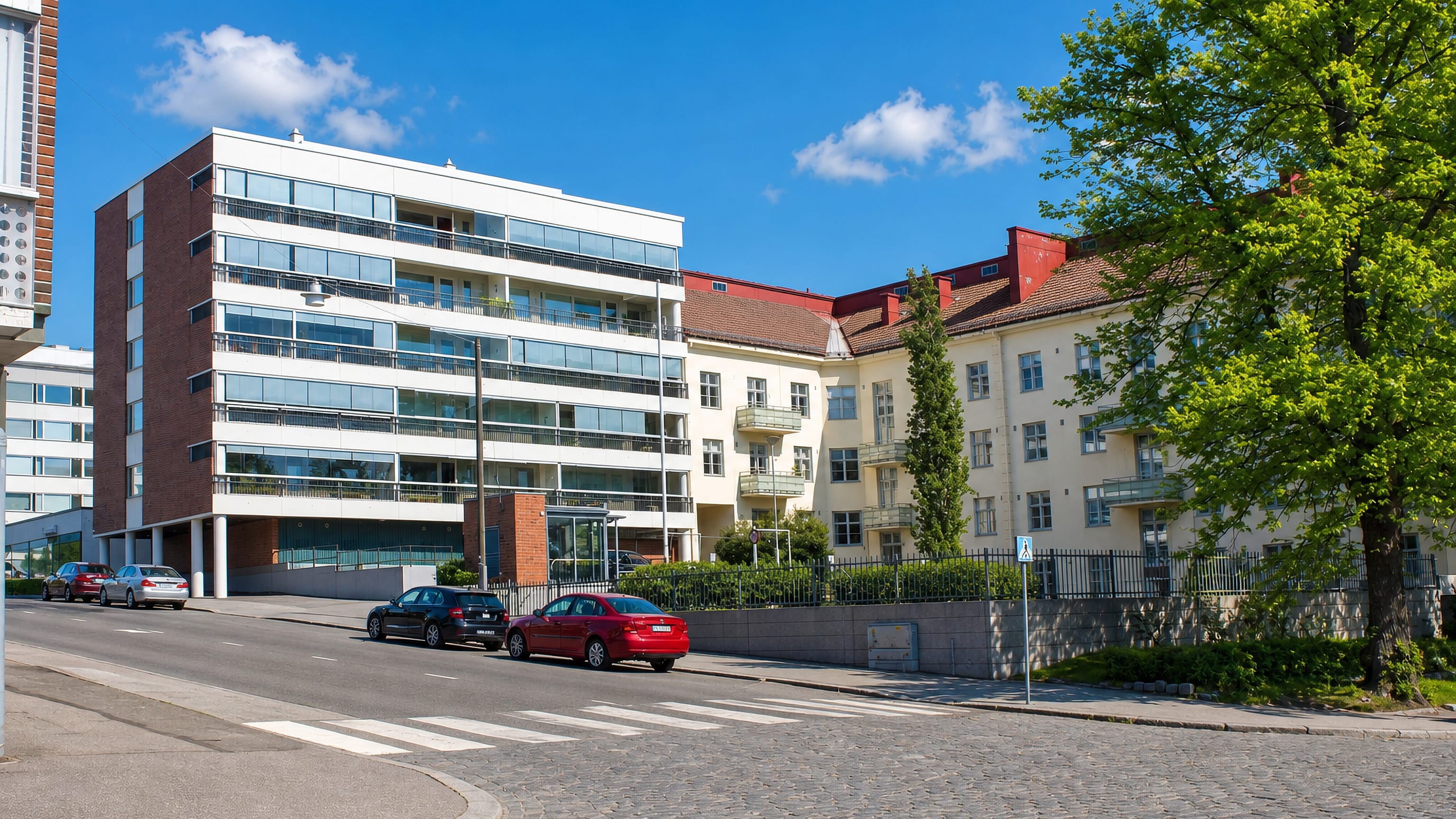Modern white apartment block beside older cream flats on a cobbled corner in VI kaupunginosa, Vaasa.