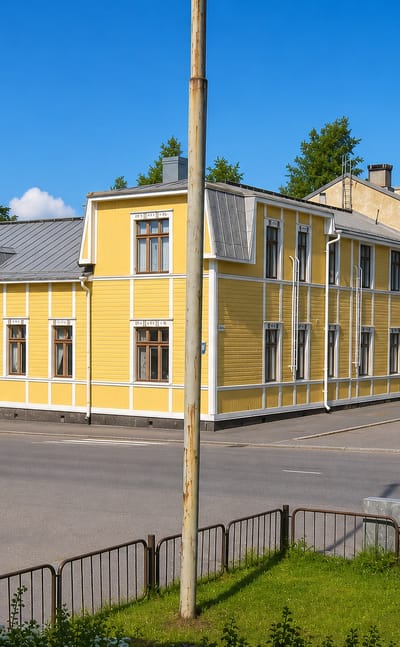 Yellow wooden houses with white trim along a quiet sunlit street in VIII kaupunginosa, Vaasa.