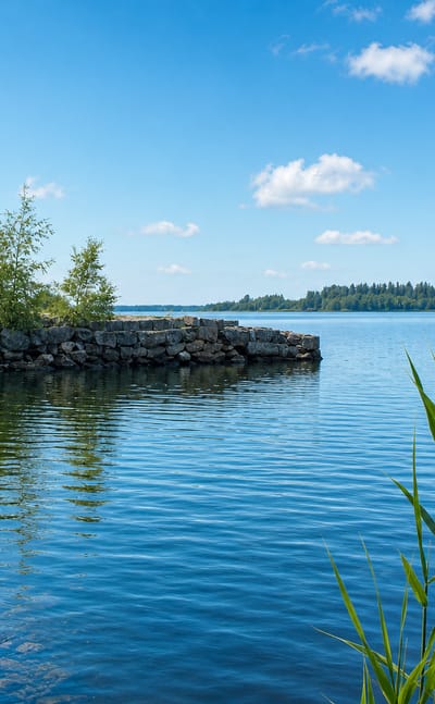 Rock-armoured shoreline and reeds on sunlit open water at Viikinlohko in Vaasa, Finland.