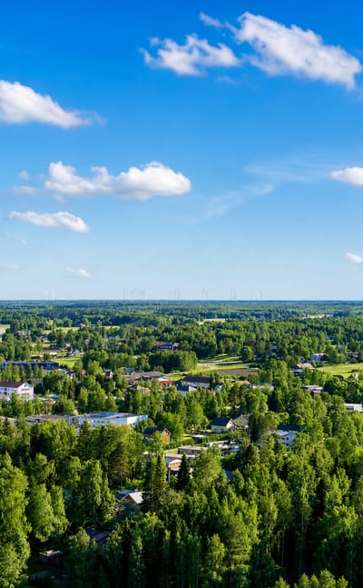 Aerial daytime view over Vörå, Finland, a low-rise village set among boreal forest and farmland under a blue sky.