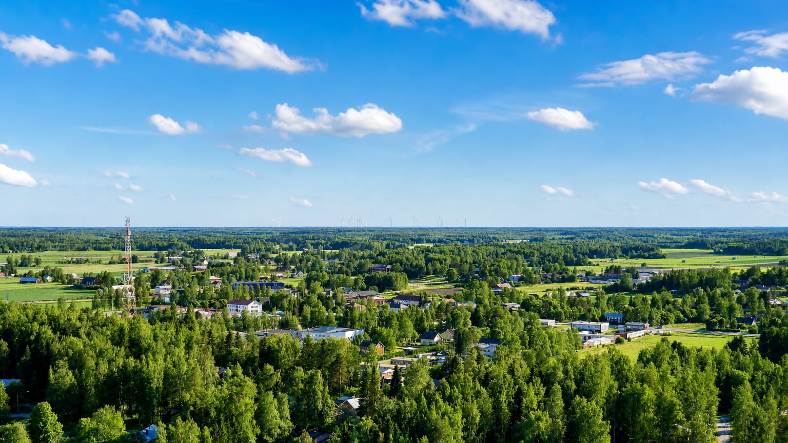 Aerial daytime view over Vörå, Finland, a low-rise village set among boreal forest and farmland under a blue sky.