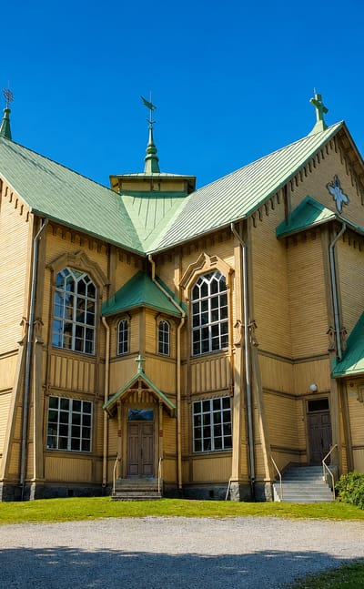 Ornate yellow wooden church with a green roof and Gothic windows under a blue sky in Heinävesi, Finland.