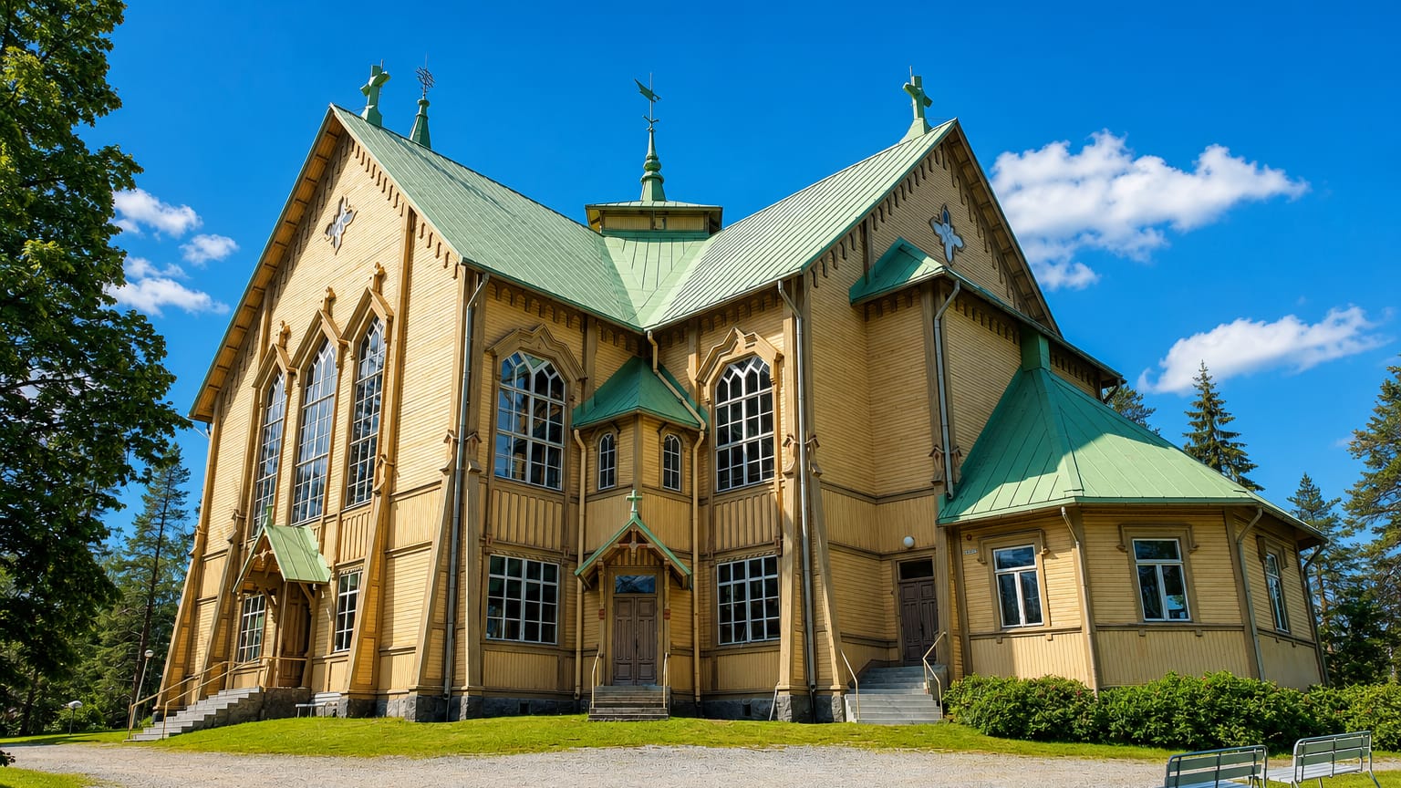 Ornate yellow wooden church with a green roof and Gothic windows under a blue sky in Heinävesi, Finland.