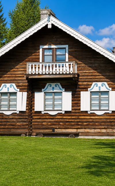 A traditional Karelian log house with carved white shutters and a balcony in Ilomantsi, Finland.